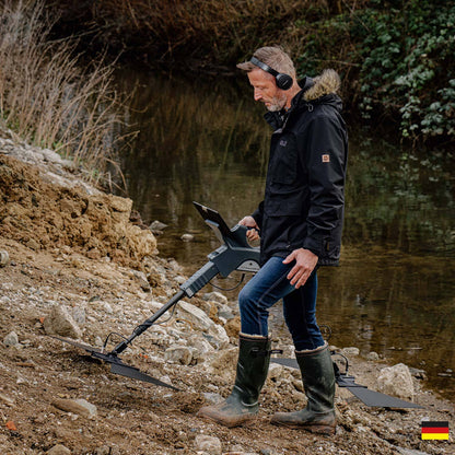 Man with a metal detector by a water body